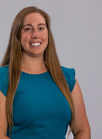 "A woman wearing a teal blue top is smiling at the camera"