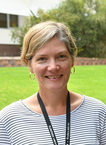 A woman with short blonde hair stands outside on a lawn. 