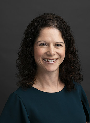 A woman with curly brunette hair is in front of a dark background. 