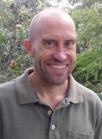 A bald man wearing a grey shirt looks at the camera