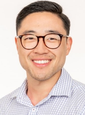 "An Asian man wearing black framed glasses is smiling at the camera"