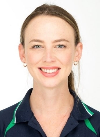 "A woman wearing a navy blue and green polo shirt is looking at the camera. Her hair is pulled back into a ponytail. 