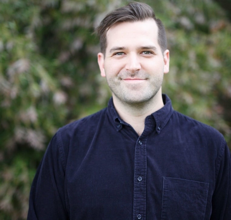 "A man wearing a dark blue shirt is standing in front of a bush."