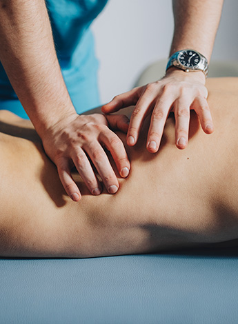 A therapist's hands are massaging the torso of a person lying on a massage table. Only their torso can be seen. 