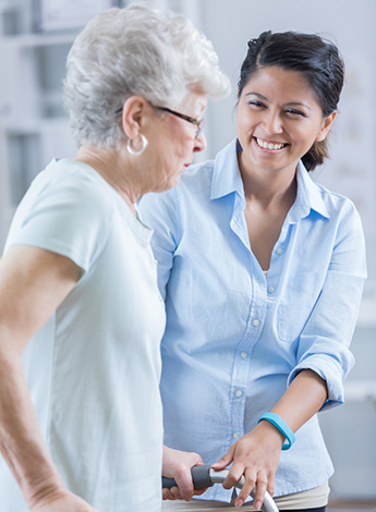 ""older woman with walking frame being assisted by physiotherapist