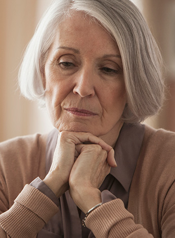 Older woman rests chin on hands, looking sad.